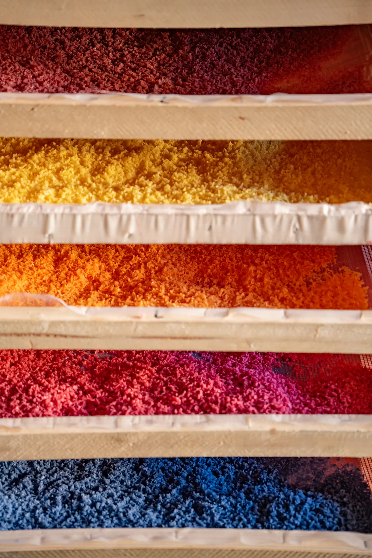 Gefärbte Wachsspäne in Rot, Gelb, Orange, Pink und Blau auf Holzgestellen zum Trocknen