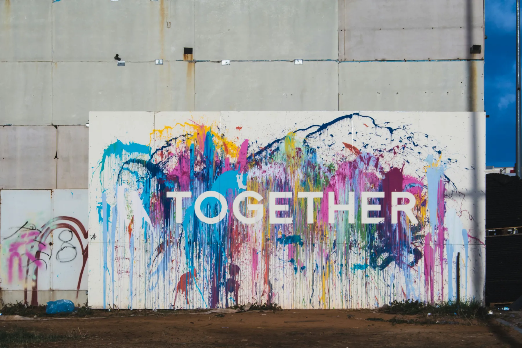 Ein Wandbild mit dem Wort TOGETHER, darüber bunte Farbläufe auf einer Betonwand